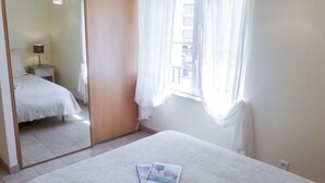 Una camera da letto con un letto, un comodino, una lampada, una finestra con tende e uno specchio che riflette l'ambiente.