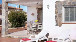 Un espace patio avec une table et des chaises, un coin détente au bord de la piscine avec des transats, et un mur en pierre.