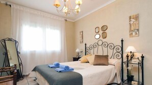 Une chambre à coucher bien rangée, avec un lit, des lampes de chevet, un miroir et une petite table sur laquelle est posée une plante.