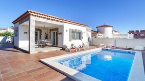 Une maison avec une piscine, une terrasse avec des chaises et un toit recouvert de tuiles.