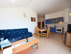 A compact living space with a blue sofa, wooden dining table, and a kitchenette with blue cabinets.