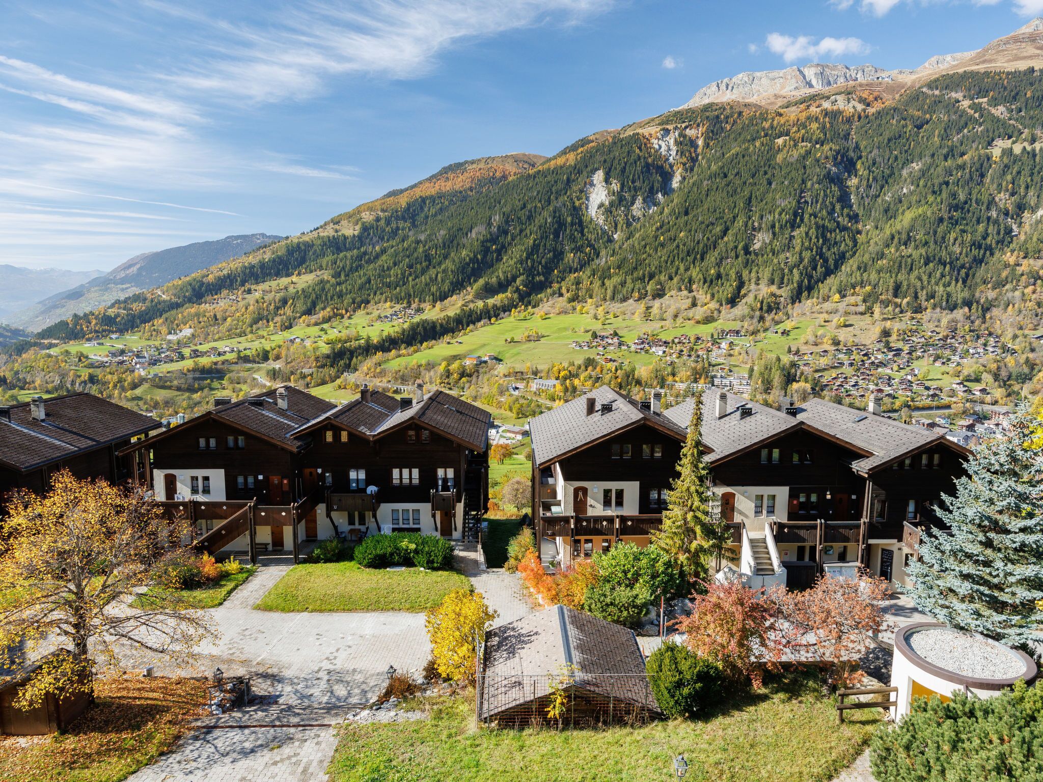 A mountain village with traditional wooden houses, a paved pathway, and a view of the surrounding hills and mountains.