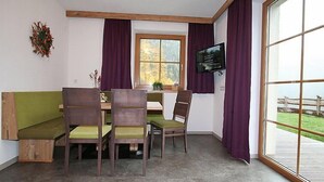 A room with a wooden table, four chairs, a television, a window with curtains, and a view of a wooden fence. - s ´ HimmelReich by Interhome (Längenfeld)