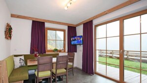 A cozy room with a wooden bench, a table, and chairs. There's a TV on the wall and a large window with a view of the outdoors. - s´ HimmelReich by Interhome (Längenfeld)