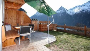 A wooden deck with a table and chairs, a green umbrella, and a mountain view. - s´ HimmelReich by Interhome (Längenfeld)