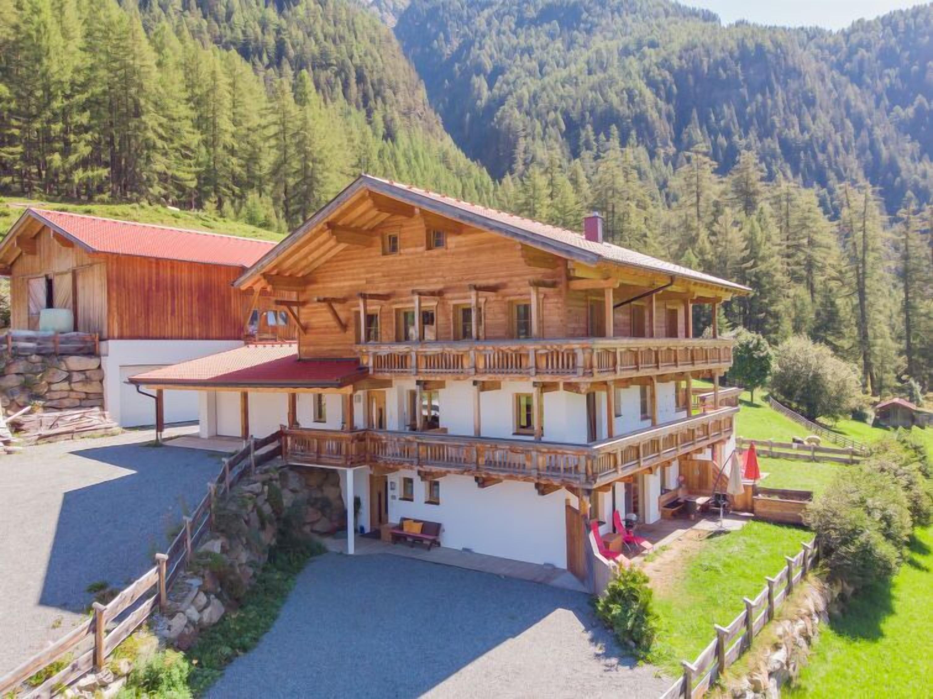Un chalet en bois à deux étages, doté d’un balcon, situé dans une région montagneuse couverte de forêts denses.