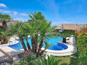 Ein Poolbereich mit Palmen, einem Whirlpool und einem ziegelgedeckten Gebäude im Hintergrund.