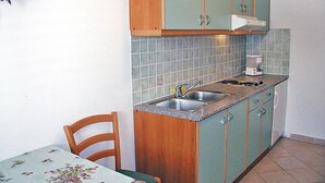A small kitchen with two sinks, wooden cabinets, and a table with a floral tablecloth. - Apartment Zdenko by Interhome (Ugljan/Kali)