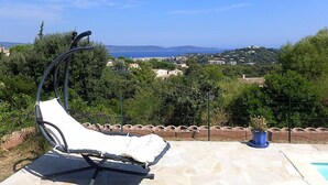 A sun lounger on a stone patio overlooking a coastal landscape with houses and greenery.