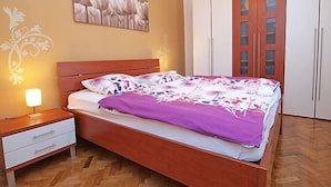 A bedroom with a wooden bed, white nightstands, a wall-mounted light, a floral painting, and a wardrobe with glass doors. - Apartment Ante by Interhome (Brodarica)