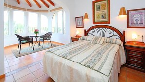 A bedroom with a large bed, a dining table with chairs, and a view through a window. - Vacation home Inma by Interhome (Pego)