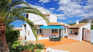 A white house with a tiled patio, a blue awning, and a palm tree. - Vacation home Inma by Interhome (Pego)
