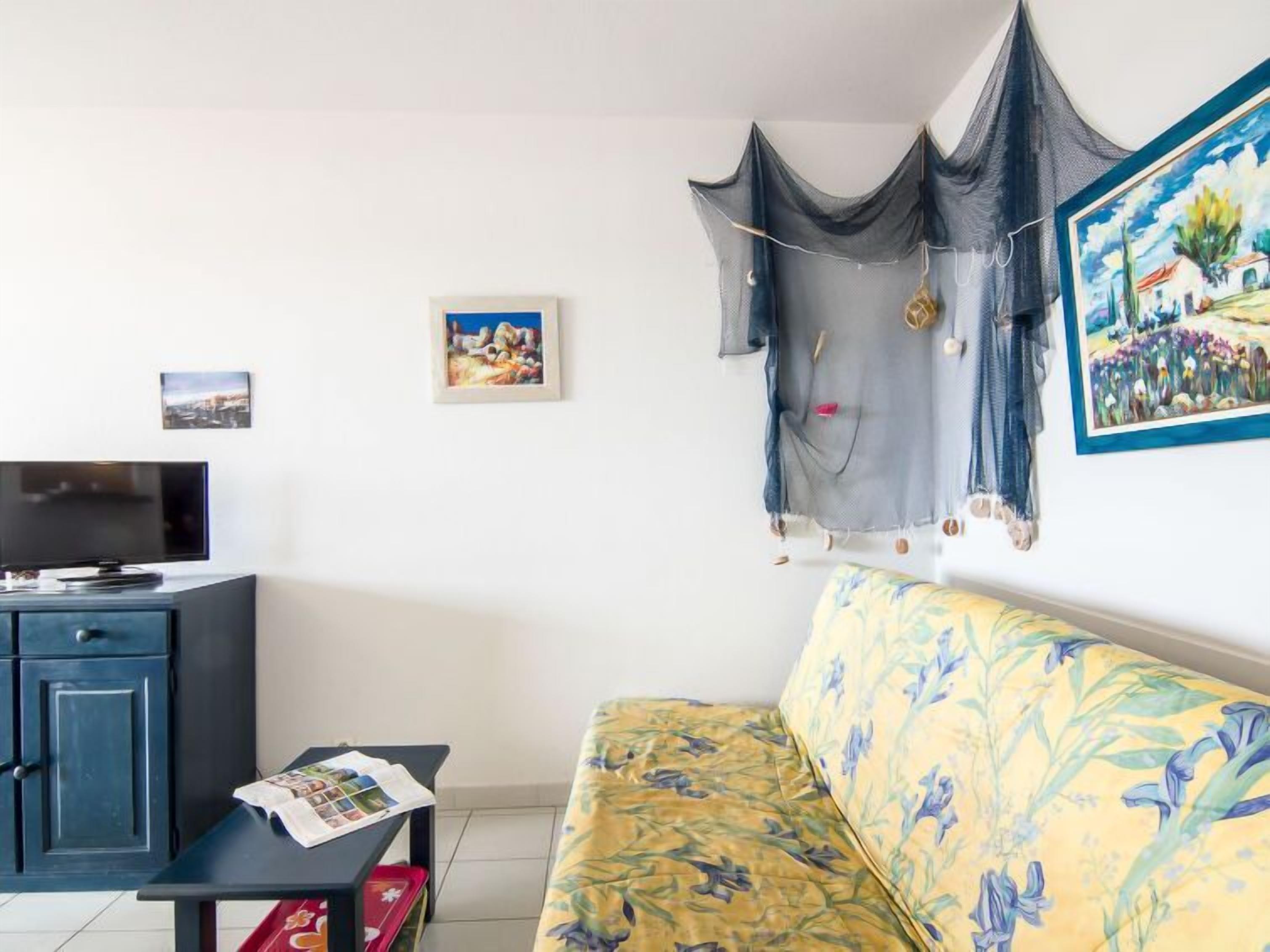 Un soggiorno con un divano, una TV, un tavolino con riviste e una parete decorata con due quadri.