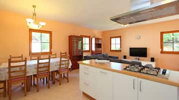 A modern kitchen with a dining area, wooden cabinets, a built-in oven, and a TV.