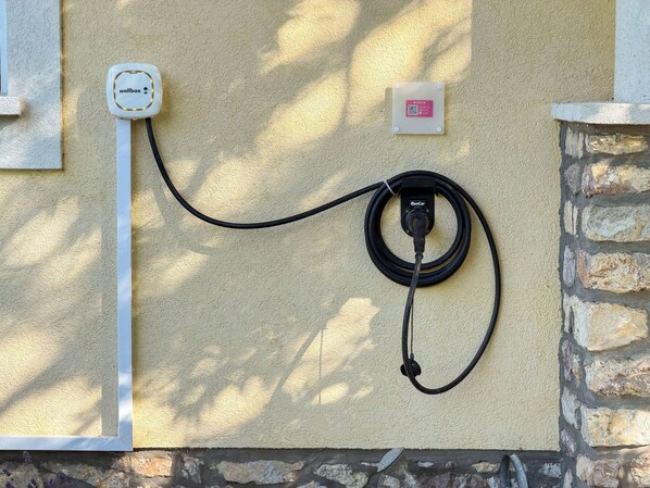 A wall-mounted charging station with a cable connected to a car charger, a wall socket, and a QR code plaque.