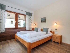 Une chambre à coucher avec un lit en bois, deux tables de chevet, une commode et une fenêtre avec des rideaux.