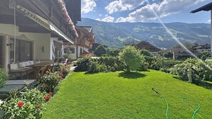 Un chalet tradicional con un jardín cuidado, cielo despejado y montañas al fondo.