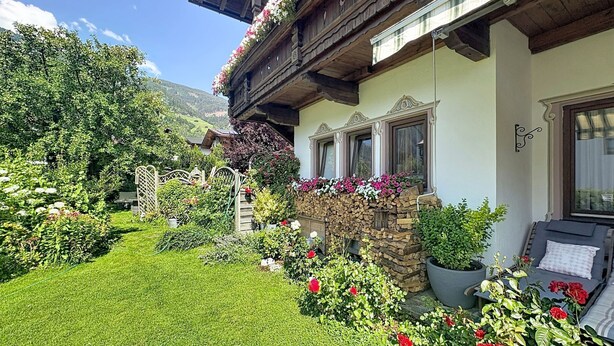 Un chalé tradicional con fachada de piedra, un balcón de madera con flores y un jardín bien cuidado.