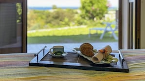 Bandeja de desayuno con un croissant, una taza y un pastel enrollado sobre una mesa junto a una ventana con vistas a zonas verdes y un banco.