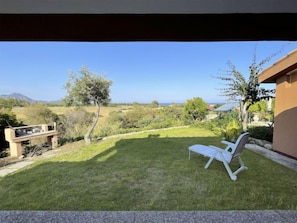 Un patio trasero con césped, una silla de descanso blanca y vistas al campo y a las montañas.