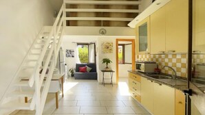 Cocina amplia con una escalera que sube a un nivel superior, un comedor con sofá y mesa, y vista a zonas verdes exteriores.
