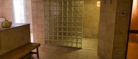 A bathroom with a bench, a glass partition, and a tiled floor.