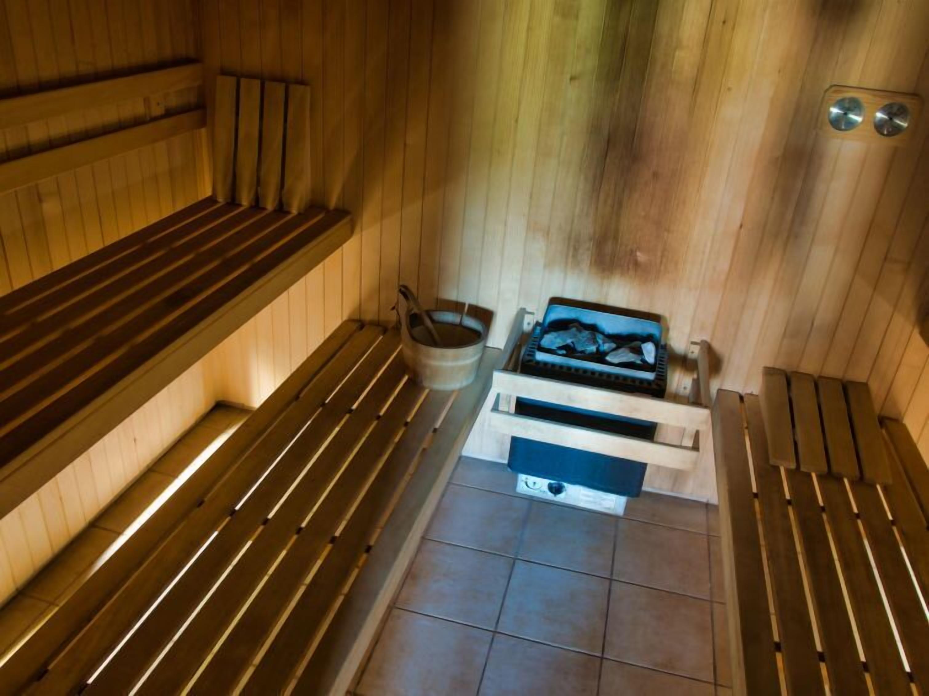 Una sauna con bancos de madera, un balde y un recipiente con piedras.
