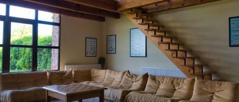 A spacious living room with a large sectional sofa, a wooden coffee table, and a staircase with wooden railings.