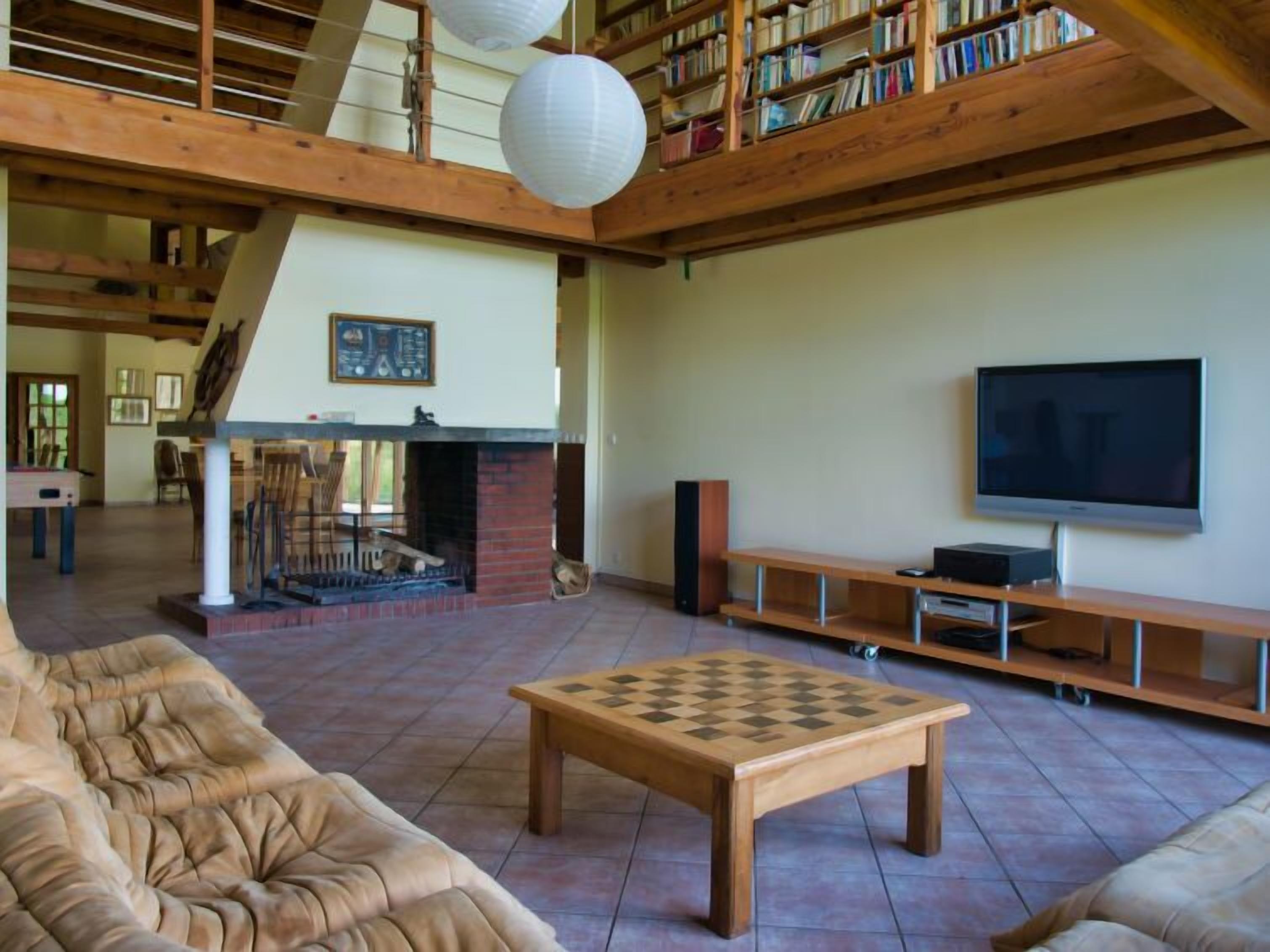 A spacious living room with a fireplace, a television, and a chess table.