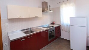 Une cuisine avec des meubles blancs, un évier à deux bacs, une cuisinière et un réfrigérateur.