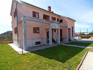 Un bâtiment à deux étages avec une façade rose, une entrée abritée et une allée menant à une voiture garée.