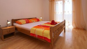 Une chambre avec un lit simple, un cadre en bois, une table de chevet avec une lampe et une fenêtre avec des rideaux légers.