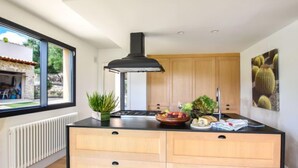 Una cocina moderna con una isla central, armarios de madera, una campana extractora negra y un amplio ventanal con vistas al exterior.