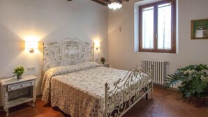 Ein Schlafzimmer mit Bett, Nachttischen, Heizkörper, Fenster und einer Pflanze.