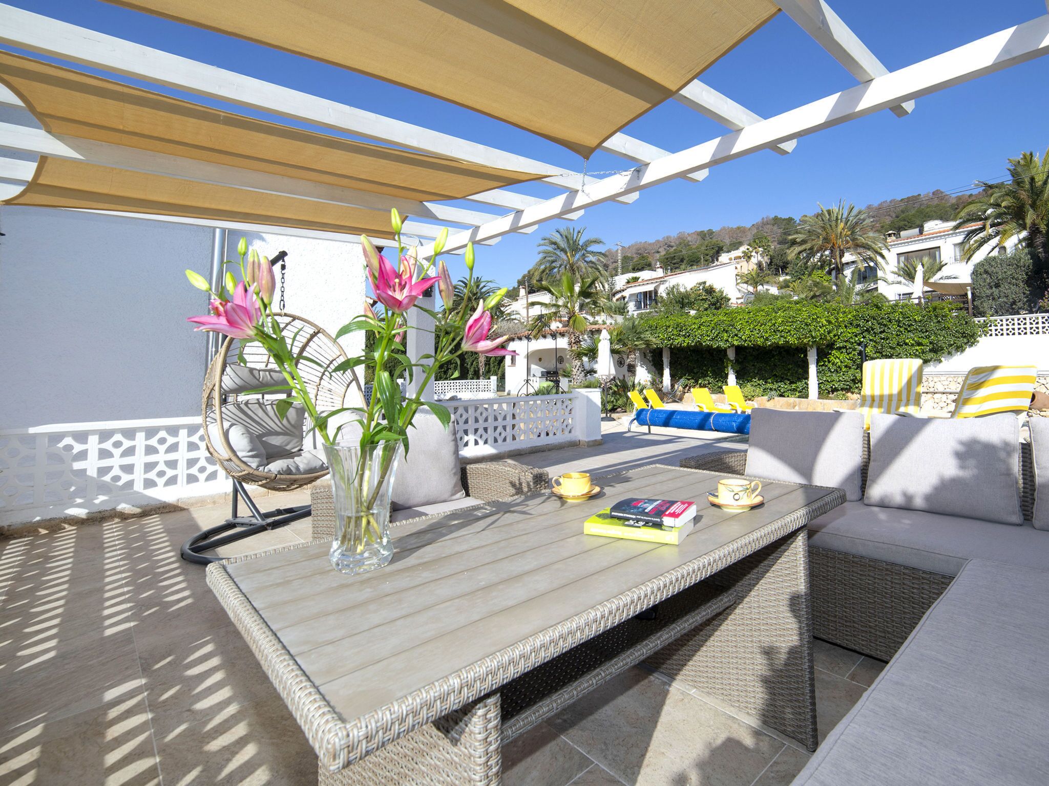 Eine Terrasse im Freien mit Korbmöbeln, einem Tisch mit Blumenvase und Blick auf die umliegende Landschaft.