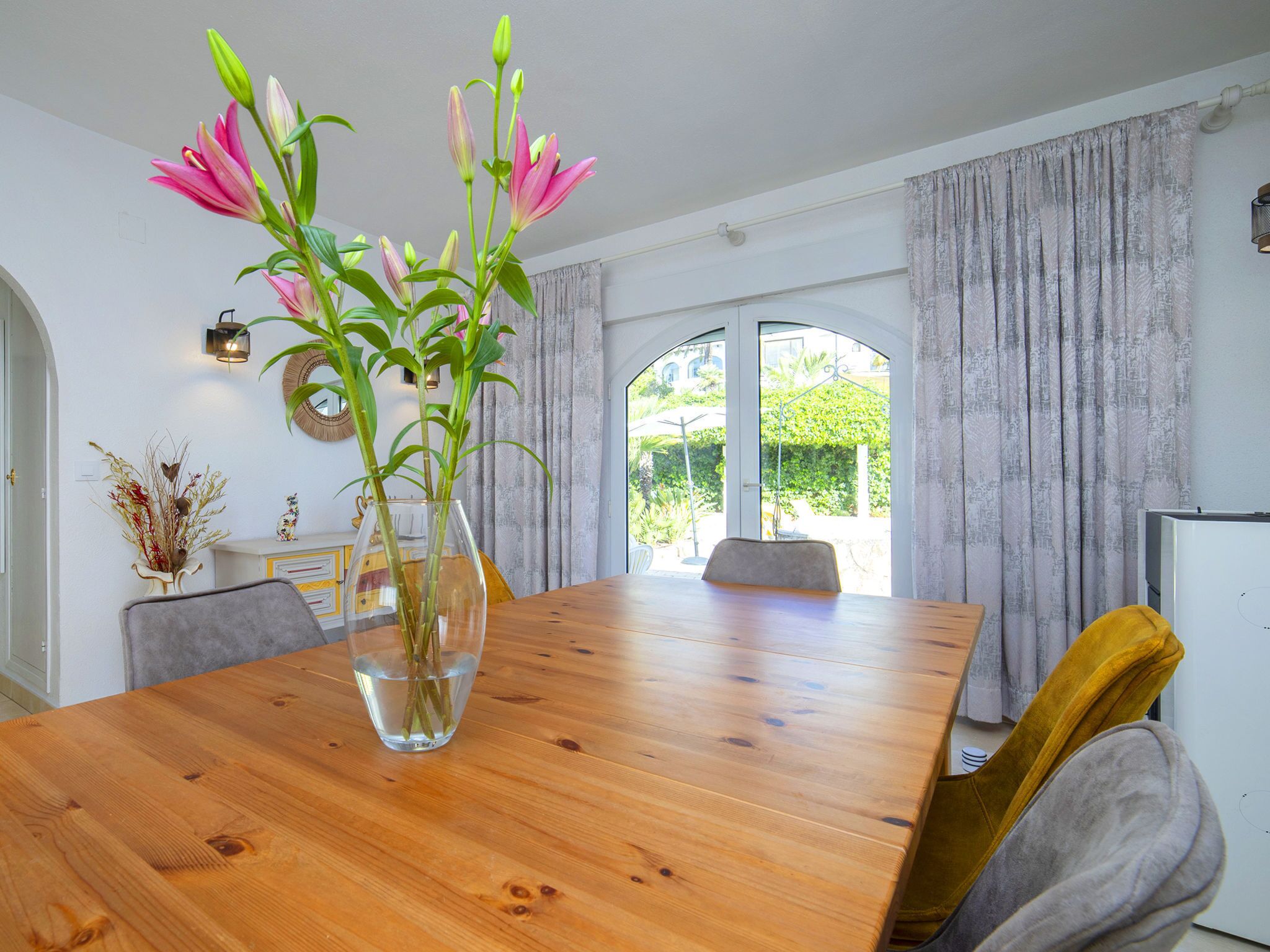 A dining area with a wooden table, chairs, and a vase with flowers.