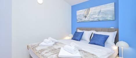 Un lit bien fait, avec une couette blanche et grise, deux oreillers bleus et deux serviettes blanches posées sur le côté.