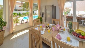 Ein Essbereich mit einem für das Frühstück gedeckten Tisch, einem Kühlschrank und Blick auf einen Swimmingpool.