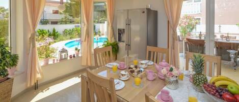 Un coin repas avec une table mise pour le petit-déjeuner, un réfrigérateur et une vue sur une piscine.