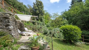 Un mur de pierre agrémenté d’une terrasse en bois, de sièges d’extérieur et de plantes en pot, le tout dans un jardin luxuriant.