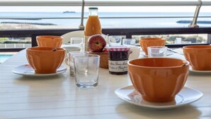 Ein Tisch ist gedeckt mit orangenen Bechern, einem Glas und einer Saftflasche, mit Blick auf ein Gewässer.
