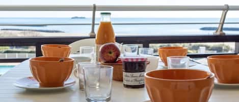 Ein Tisch ist gedeckt mit orangenen Bechern, einem Glas und einer Saftflasche, mit Blick auf ein Gewässer.