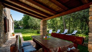 An outdoor patio with a wooden table and benches, surrounded by stone walls and a grassy area with trees. - Vacation home Tommy by Interhome (Poreč/Nova Vas)