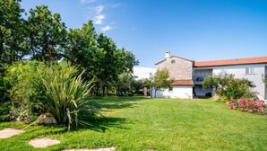 A house with a stone facade, a red-tiled roof, and a well-maintained lawn with a few trees and a large plant. - Vacation home Tommy by Interhome (Poreč/Nova Vas)