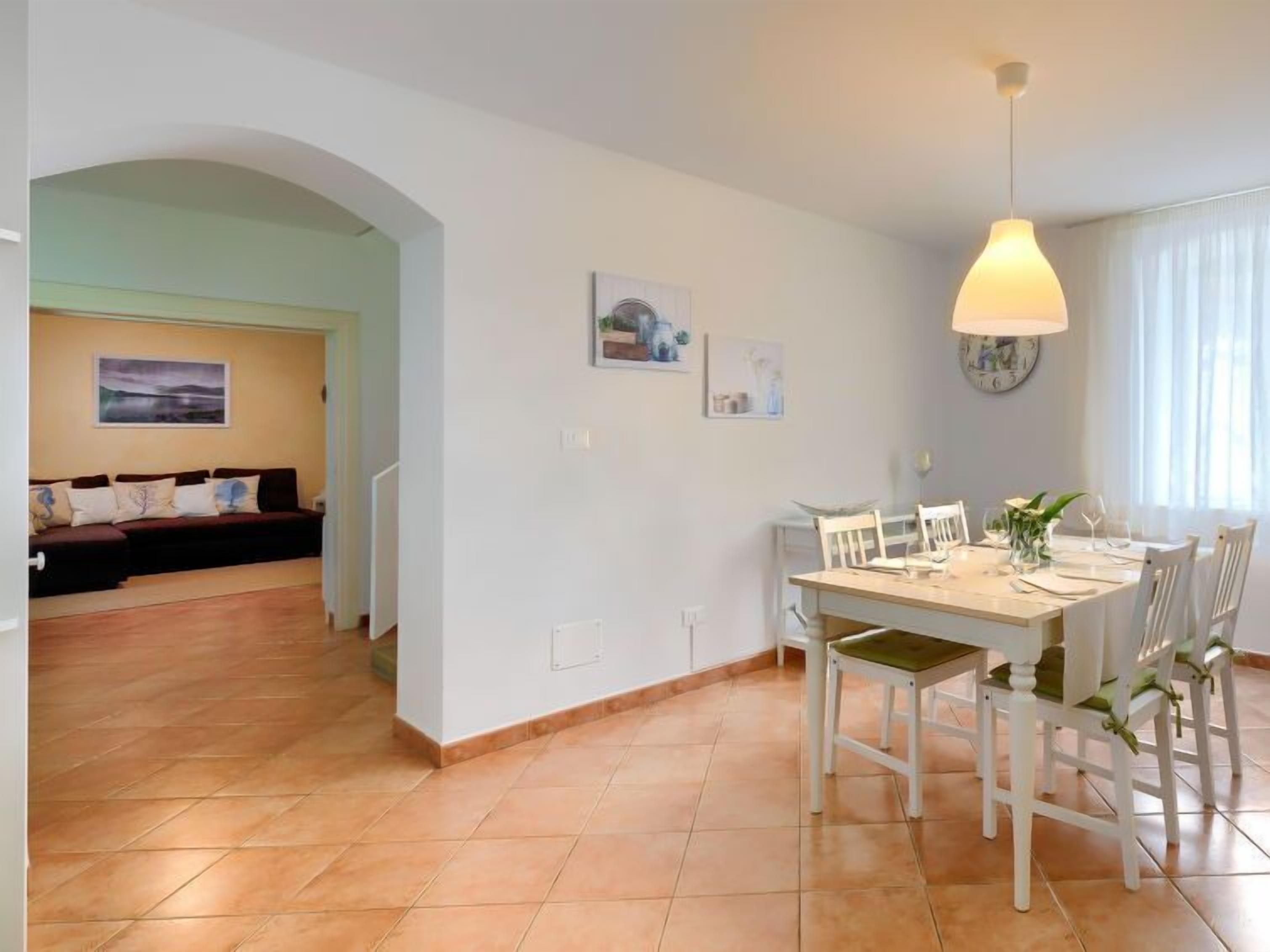 Un coin repas avec une table dressée pour quatre personnes, des chaises blanches et un luminaire suspendu.