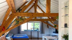 Une chambre de style « loft », avec des poutres en bois apparentes, un lit, une chaise et une petite table.