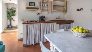 Une cuisine avec un plan de travail en marbre, une machine à café et un panier de fruits. Il y a une plante dans un coin et une fenêtre avec des rideaux.