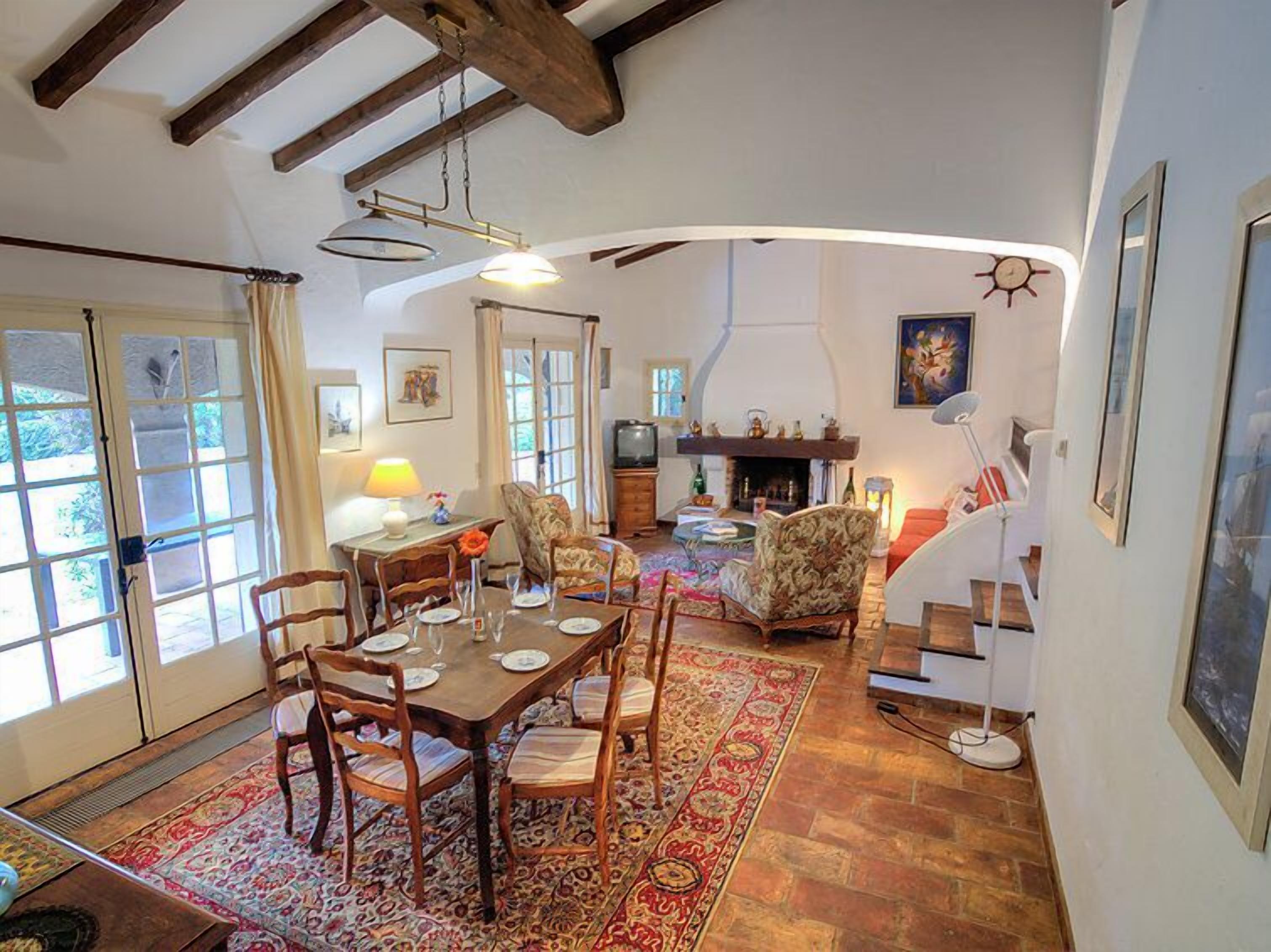 A spacious living area with a dining table set for four, surrounded by comfortable seating. A fireplace and a television are visible in the background.