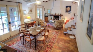 Amplia sala de estar con una mesa de comedor lista para cuatro personas, rodeada de asientos cómodos. Se aprecia una chimenea y un televisor al fondo.