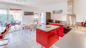 Une cuisine moderne avec des meubles de rangement rouges, une hotte de cuisine en acier inoxydable et un coin repas comprenant une table et des chaises.